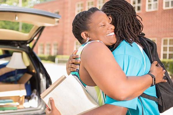 Mother hugs son goodbye in front of car loaded for moving day